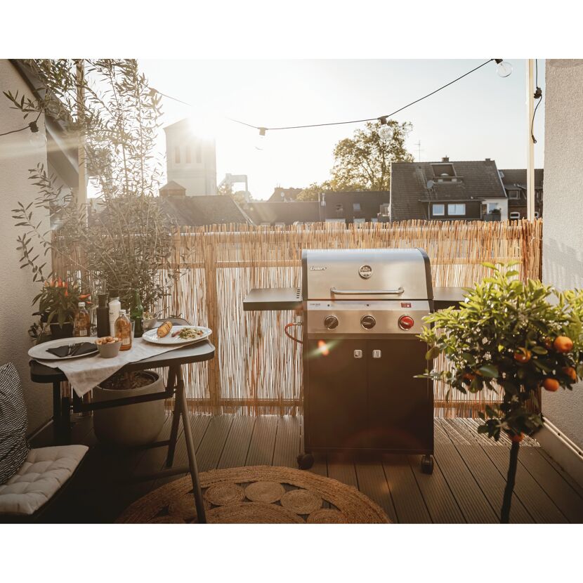Gasgrill auf einem Balkon mit Tisch und Stühlen.