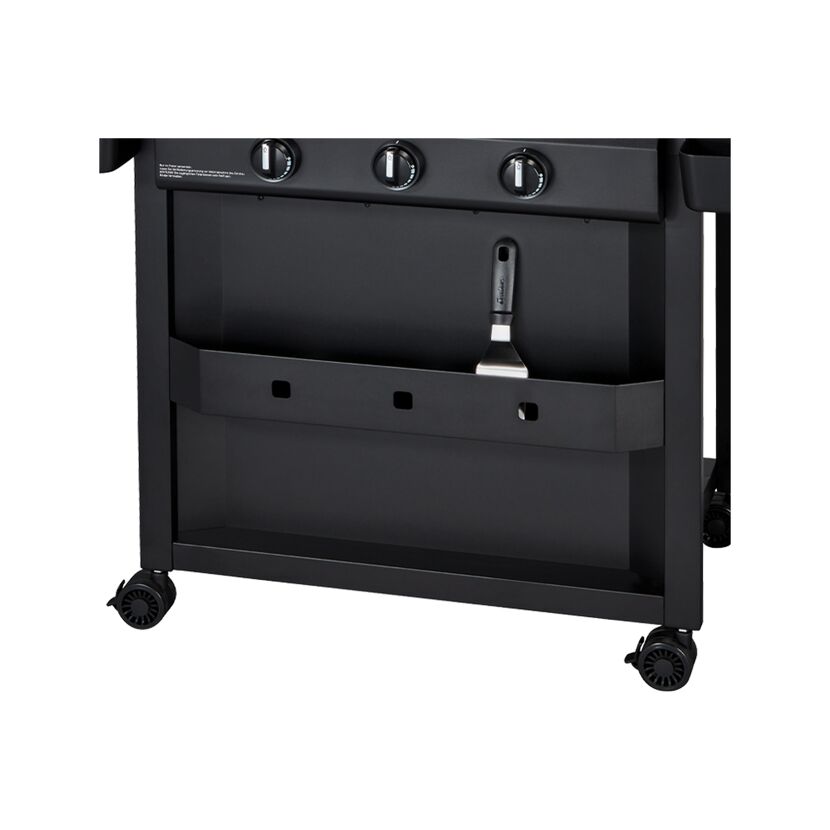 Unterseite eines schwarzen Gasgrills mit einem Spachtel.