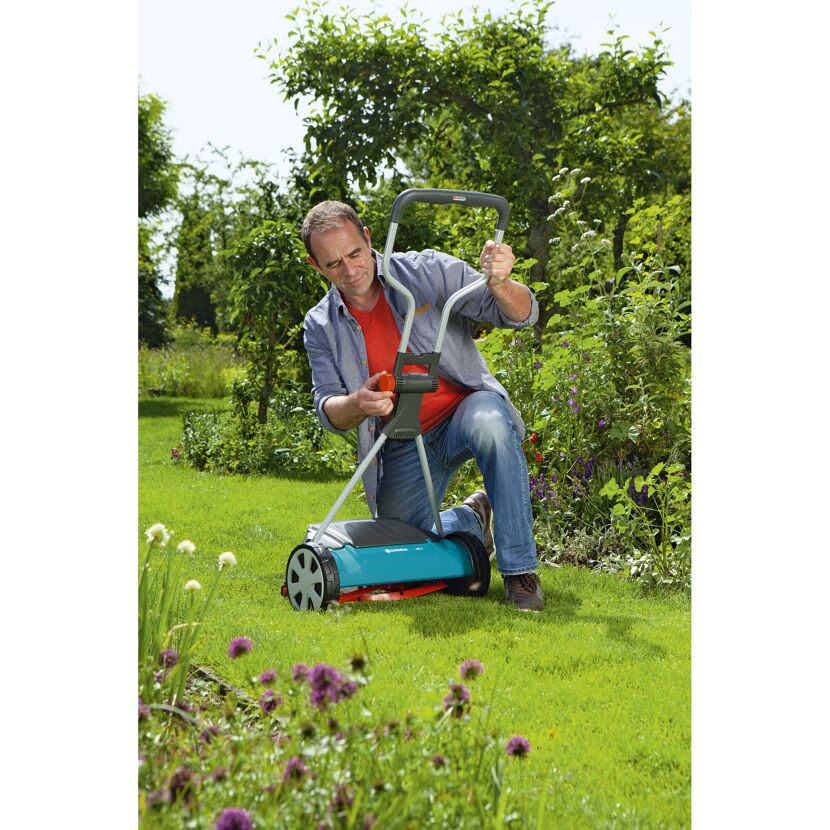 Person kniet auf einem Rasen und stellt einen GARDENA Spindelmäher ein.