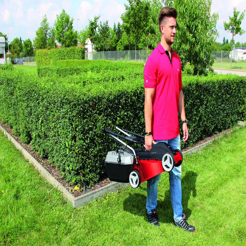 Person trägt einen roten und grauen Elektro-Rasenmäher.