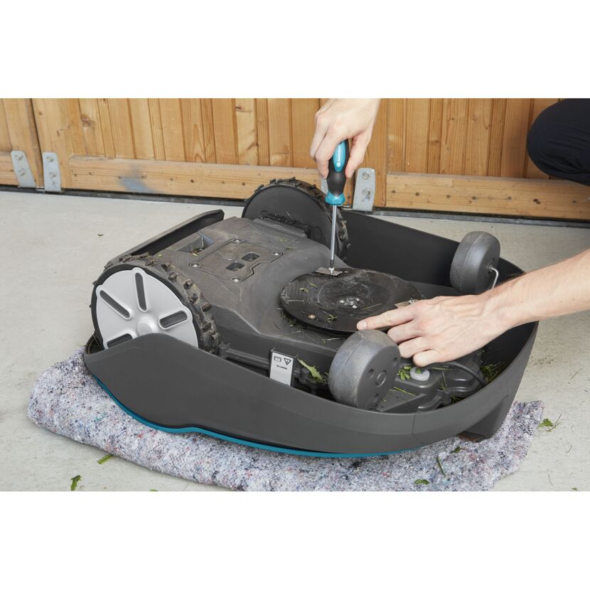 Person repariert Mähroboter mit einem Schraubenzieher.