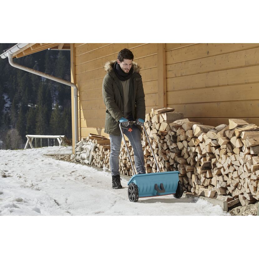 Person räumt Schnee mit einem Streuwagen