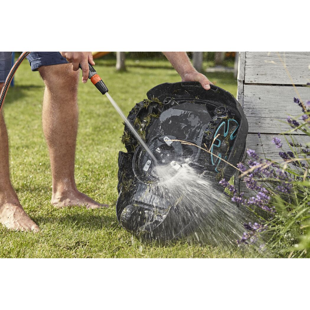 Person reinigt Mähroboter mit Wasserschlauch.