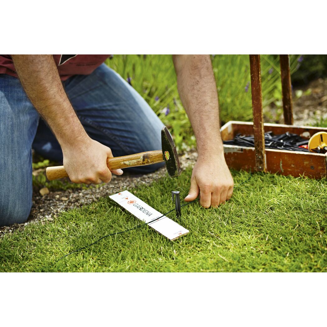 Person befestigt Begrenzungskabel mit Hammer und Nagel im Rasen.