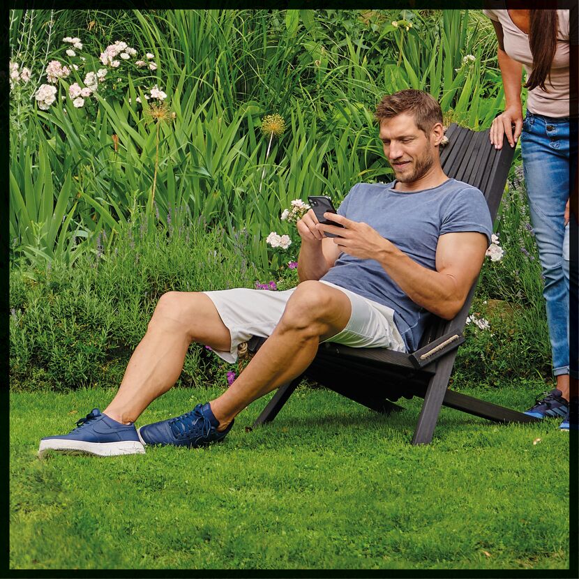 Person sitzt im Gartenstuhl und nutzt Smartphone