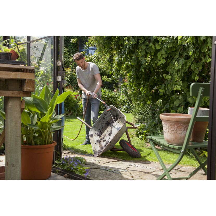 Person reinigt eine Schubkarre mit einem Gartenschlauch.