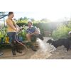 Person spritzt mit einem Gartenschlauch Wasser auf Gummistiefel und Hund