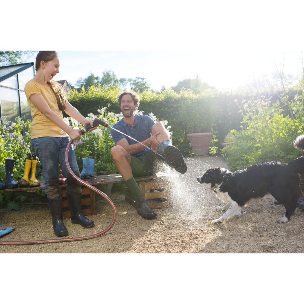 Person spritzt mit einem Gartenschlauch Wasser auf Gummistiefel und Hund