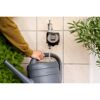 Person füllt Gießkanne mit Wasser aus einem Wasserhahn mit digitaler Bewässerungssteuerung.