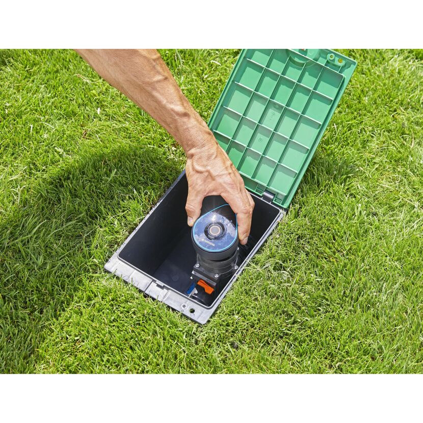 Person installiert Bewässerungssteuergerät im Garten.