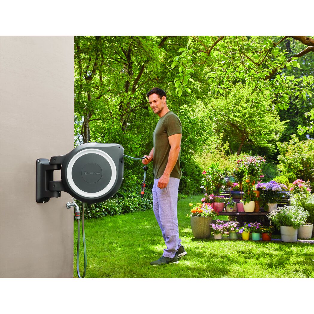 Person bewässert Blumen mit Gartenschlauch und Schlauchbox.