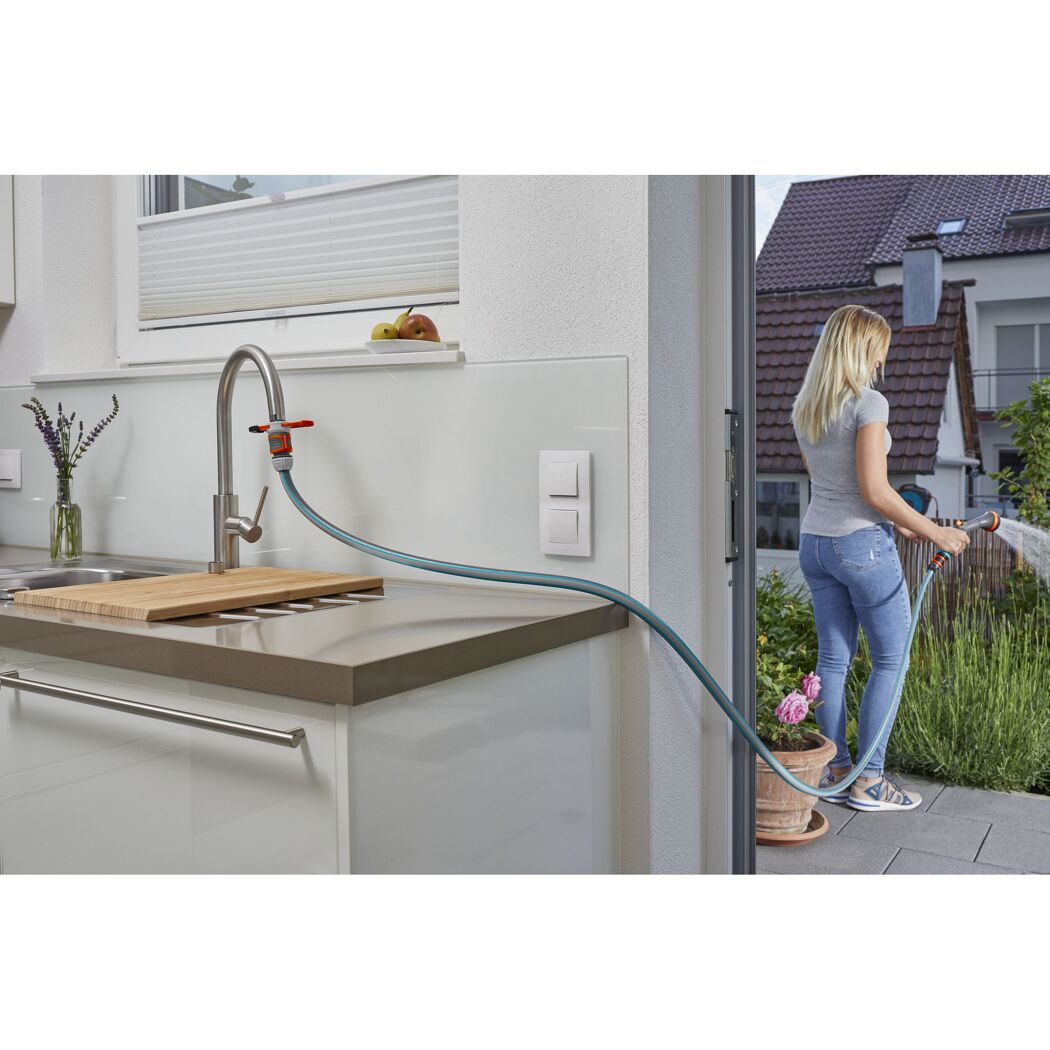 Person gießt mit Schlauch und Adapter am Wasserhahn Pflanzen.