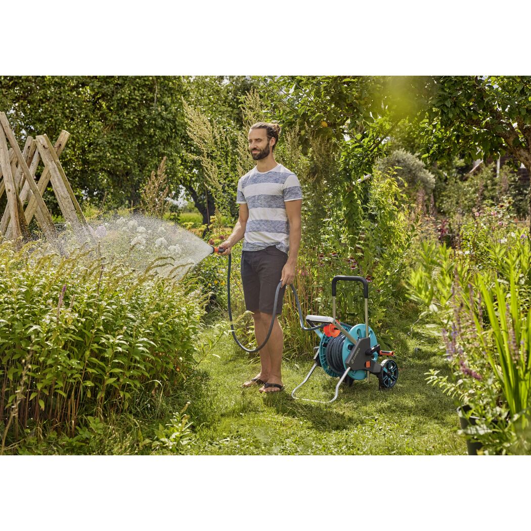 Person gießt mit Gartenschlauch und Schlauchwagen Pflanzen