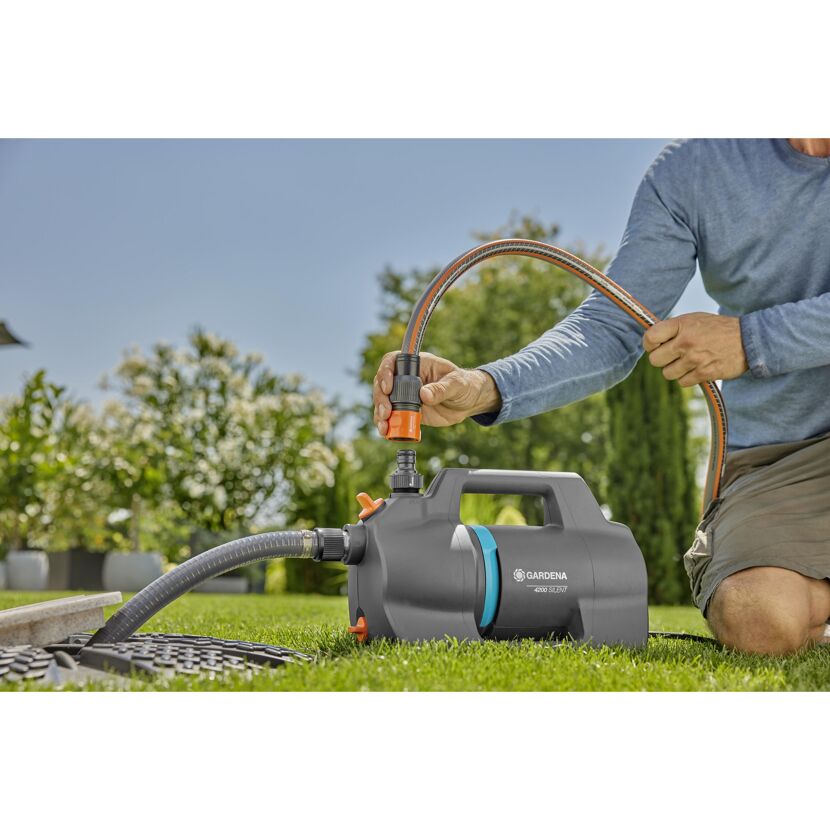 Person beim Anschließen eines Gartenschlauchs an eine Gartenpumpe.