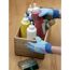 Person trägt Handschuhe und sortiert Farben und Pinsel in Holzkiste.