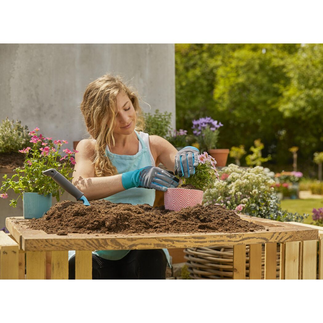Person pflanzt Blume mit Gartenhandschuhen ein