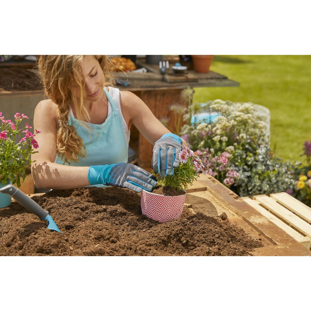 Person pflanzt Blumen mit Gartenhandschuhen ein