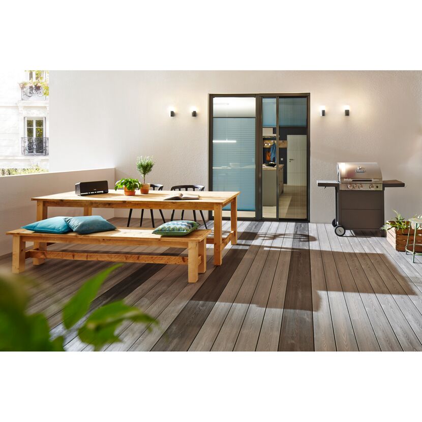 Holztisch mit Bank und Stühlen auf einem Balkon. Ein Grill steht daneben.