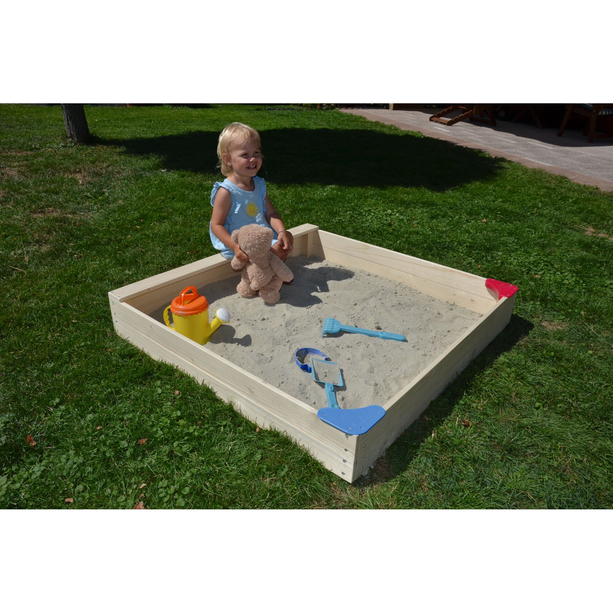 Kind sitzt in einem Sandkasten mit Gießkanne und Sandspielzeug