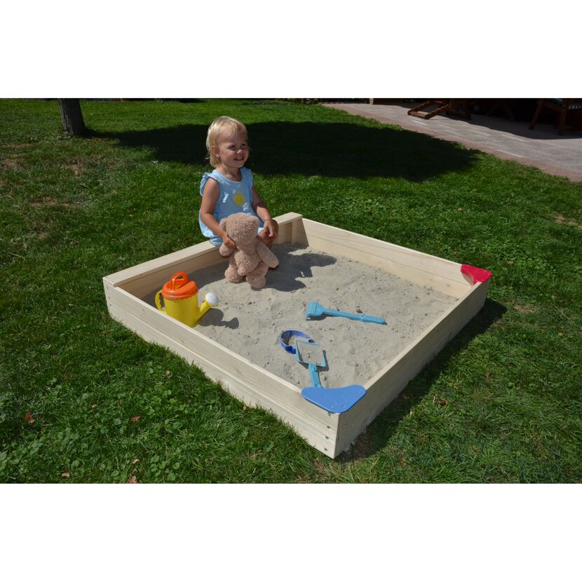 Kind sitzt in einem Sandkasten mit Gießkanne und Sandspielzeug