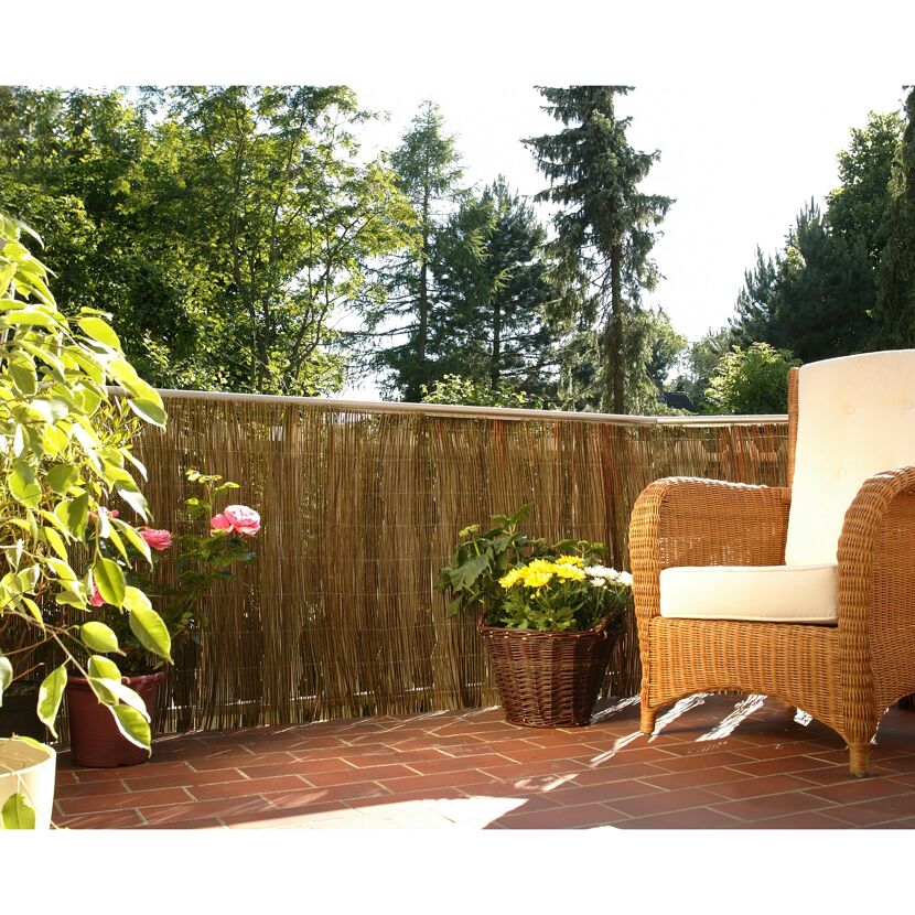 Balkon mit Weidenmatte, Korbstuhl und Blumen