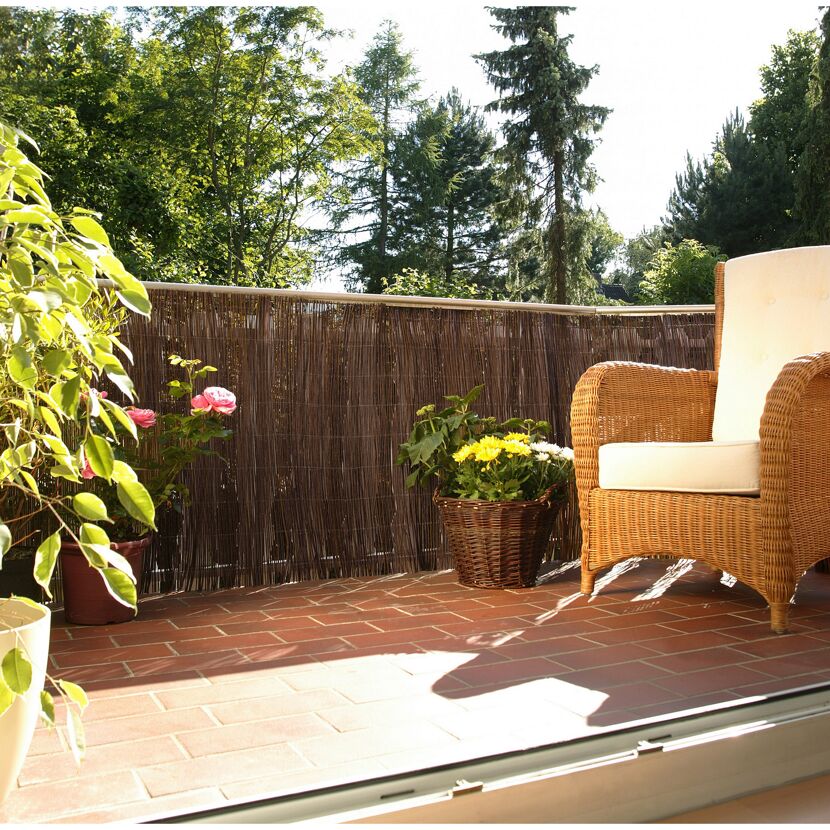 Balkon mit Farnmatte, Korbmöbeln und Blumen
