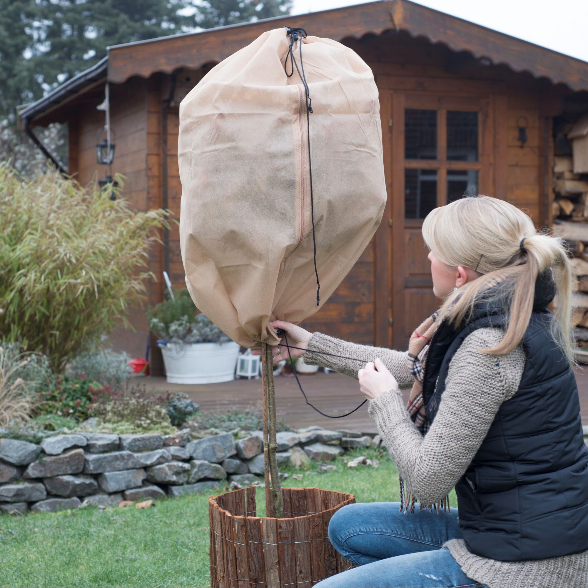 Person befestigt einen Winterschutz an einem Bäumchen