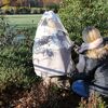 Person deckt einen Gartenbaum mit einer Vlieshaube ab.