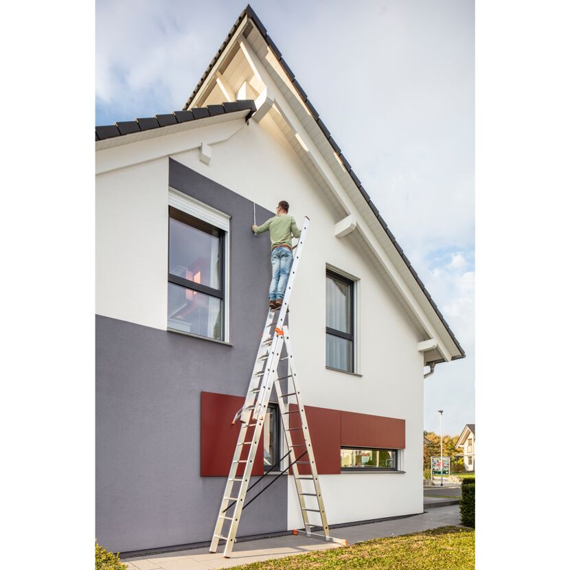 Person auf Mehrzweckleiter streicht Hausfassade