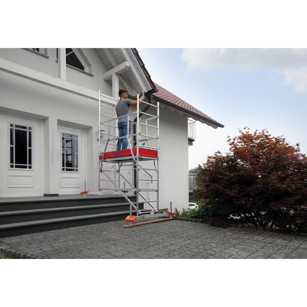 Person streicht Hauswand mit Pinsel auf einem Gerüst.