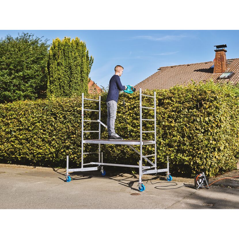 Person schneidet Hecke mit Heckenschere auf einem Gerüst.