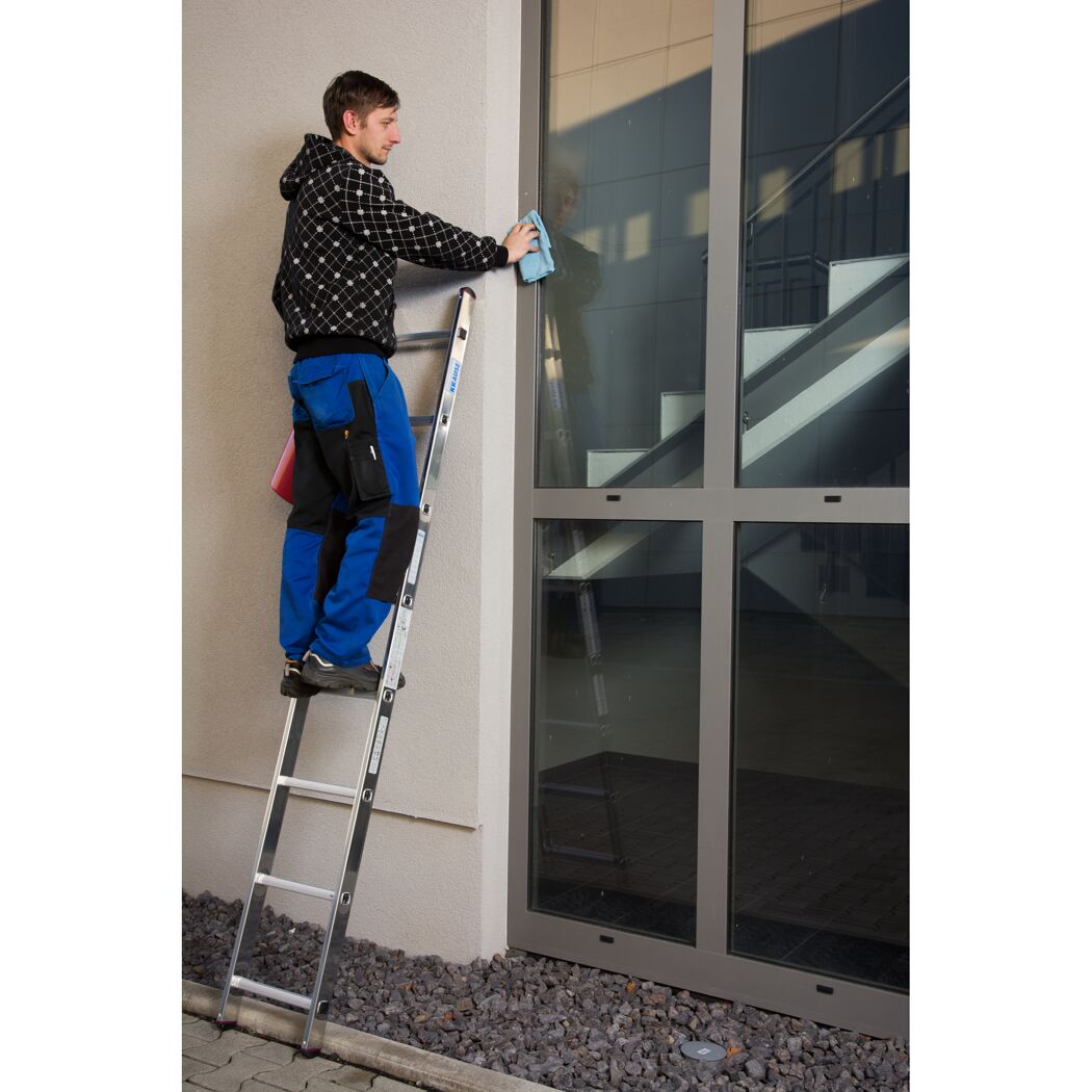 Person auf Anlegeleiter reinigt Fenster mit blauem Tuch