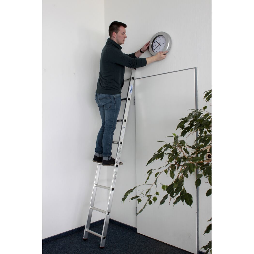 Person auf Leiter bringt Uhr an Wand an