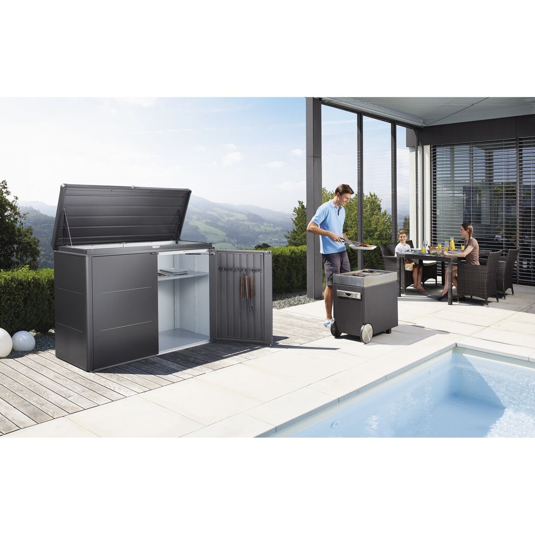 Person grillt und Familie isst an einem Tisch neben einem Pool und einer geöffneten Aufbewahrungsbox