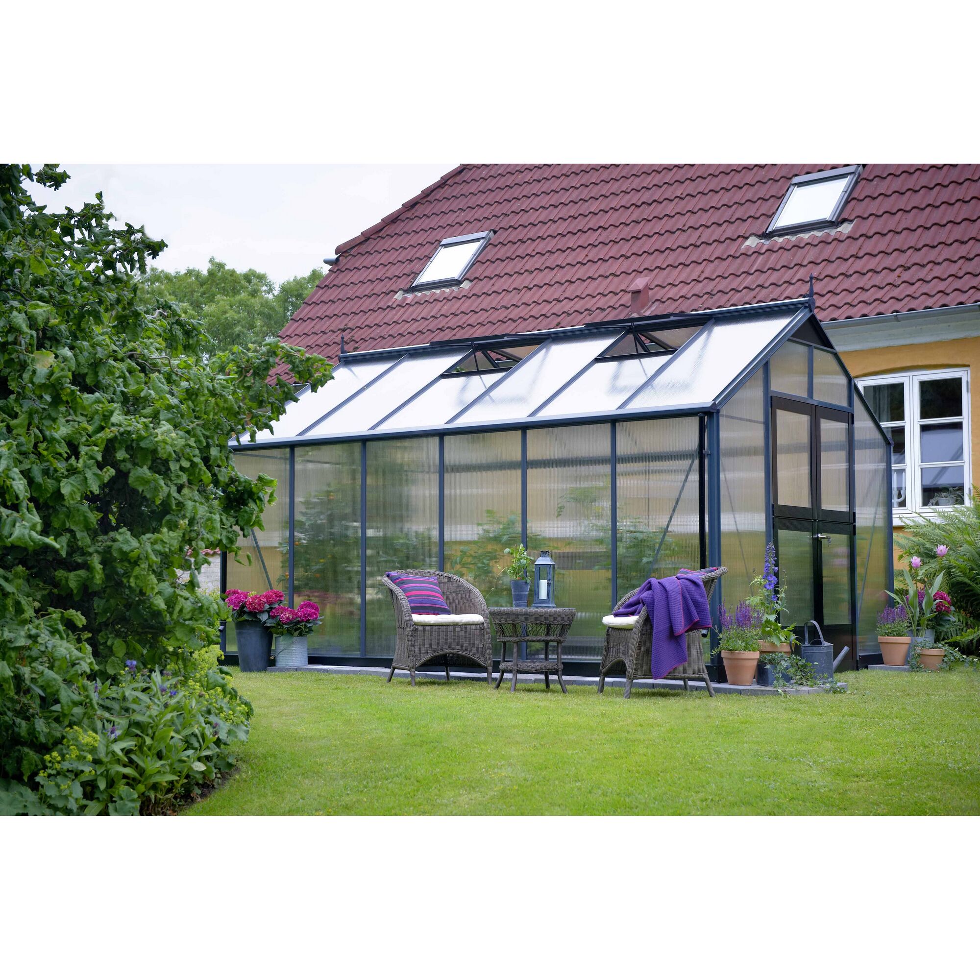 Gewächshaus im Garten mit Sitzmöbeln davor
