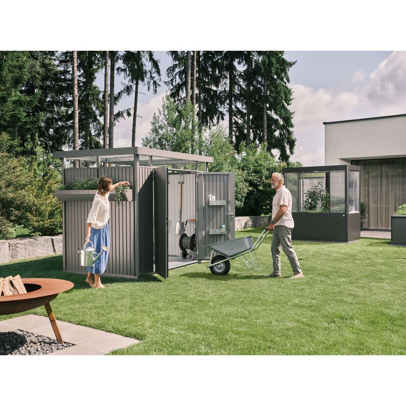 Gartenhaus 'HighLine 2' mit Gießkanne und Schubkarre im Einsatz.