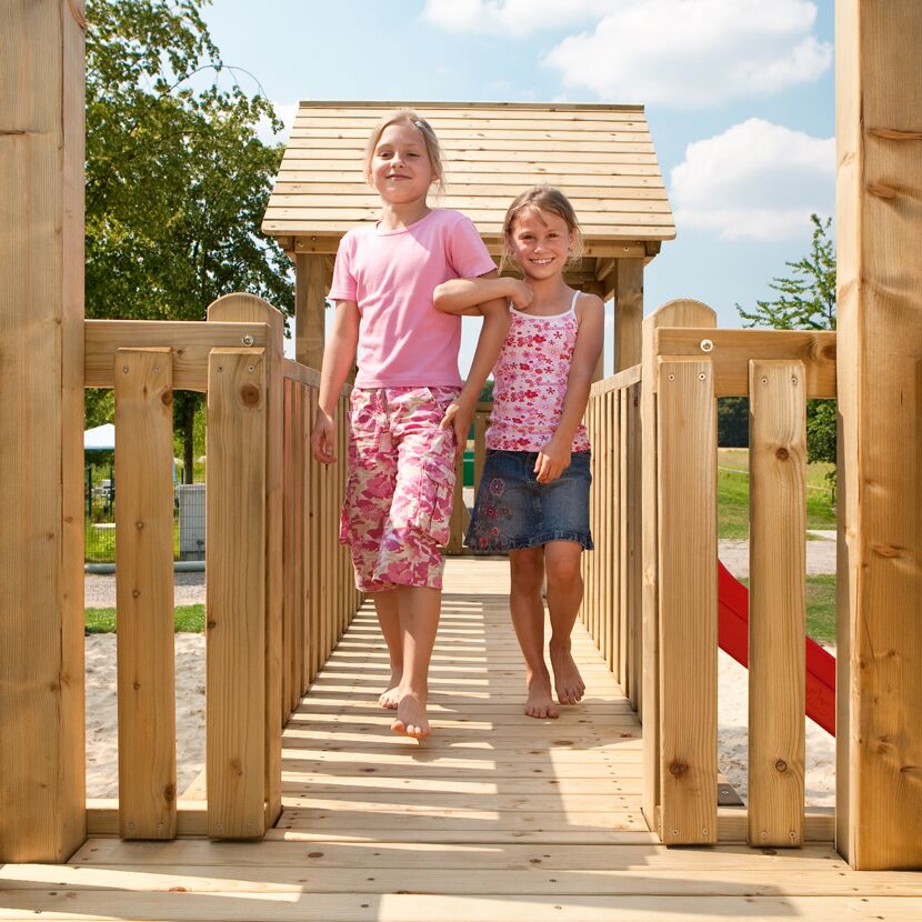 Zwei Kinder gehen barfuß über eine Holzbrücke.