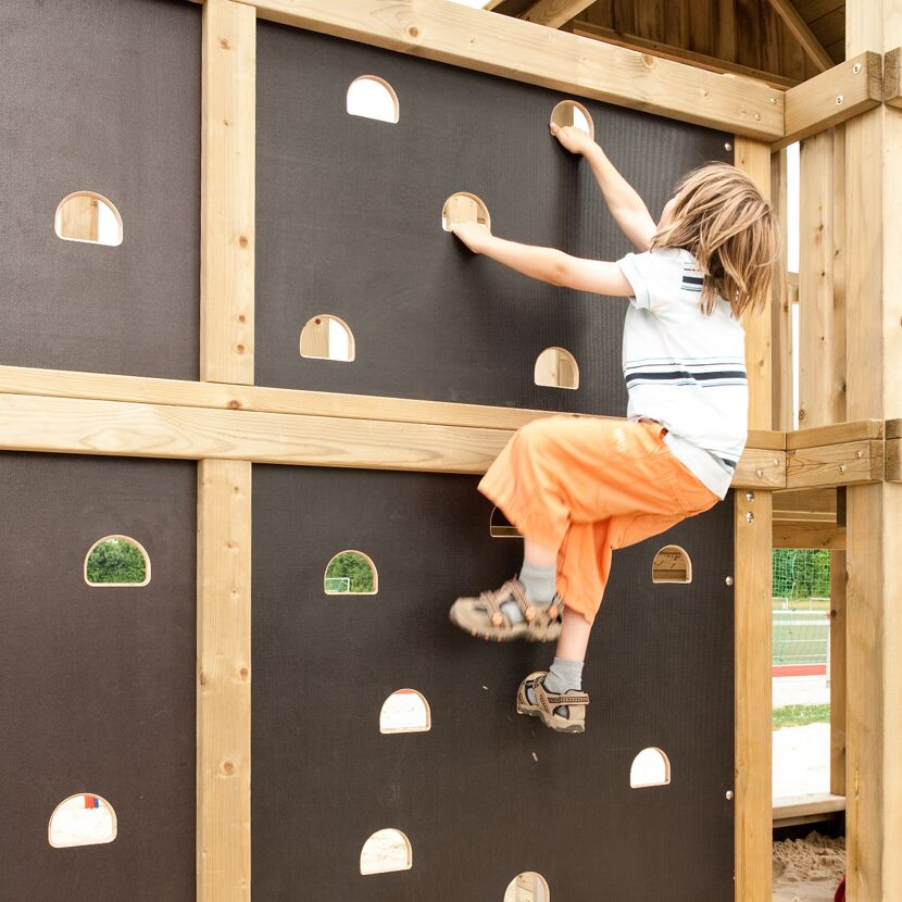 Kind klettert an Kletterwand aus Holz mit Löchern