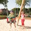 Zwei Kinder auf dem Spielplatz, eins auf einer Schaukel.