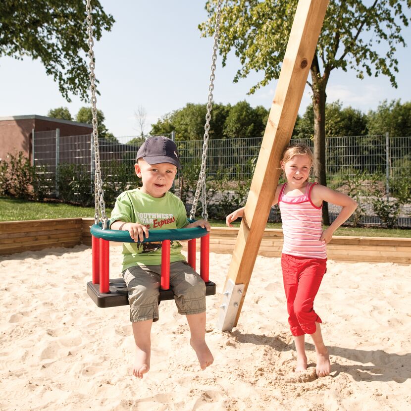 Zwei Kinder auf dem Spielplatz, eins auf einer Schaukel.