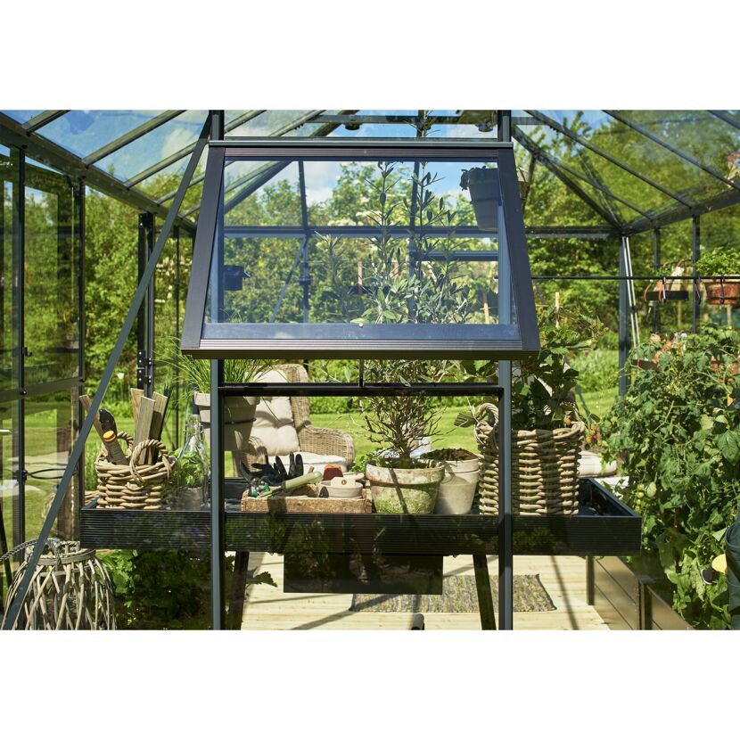 Gewächshaus mit geöffnetem Fenster, Gartenwerkzeug und Pflanzen