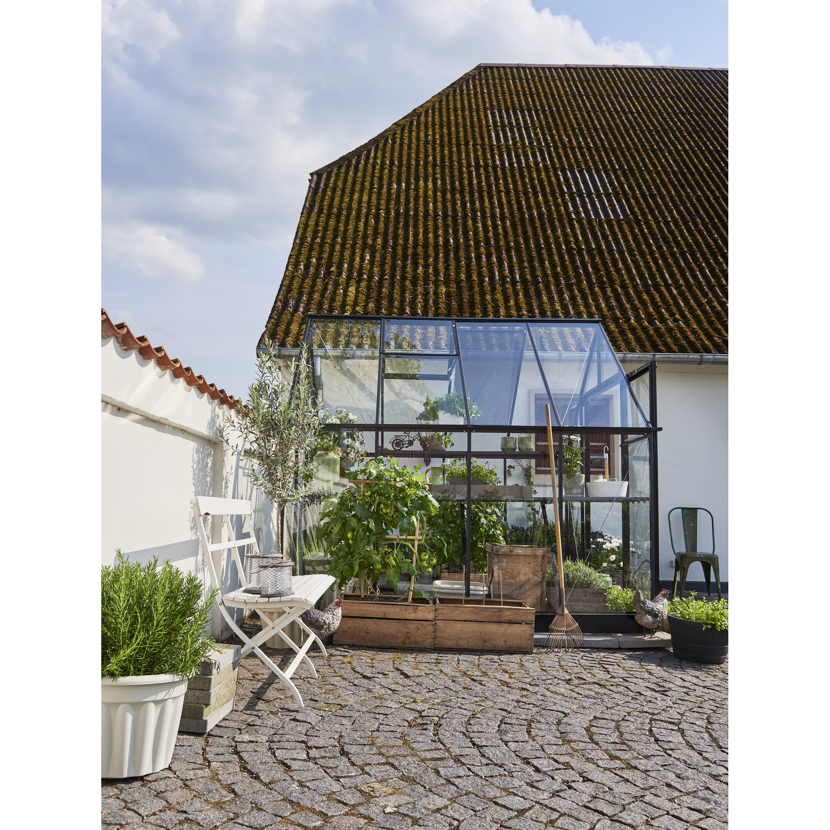 Gewächshaus im Garten mit Pflanzen und Gartenwerkzeugen