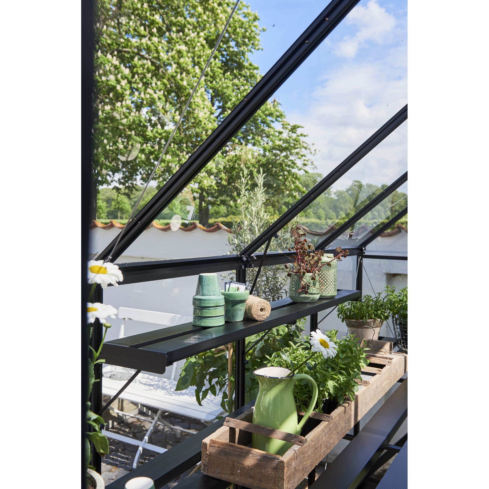 Gewächshausregal mit Blumentöpfen und Gießkanne