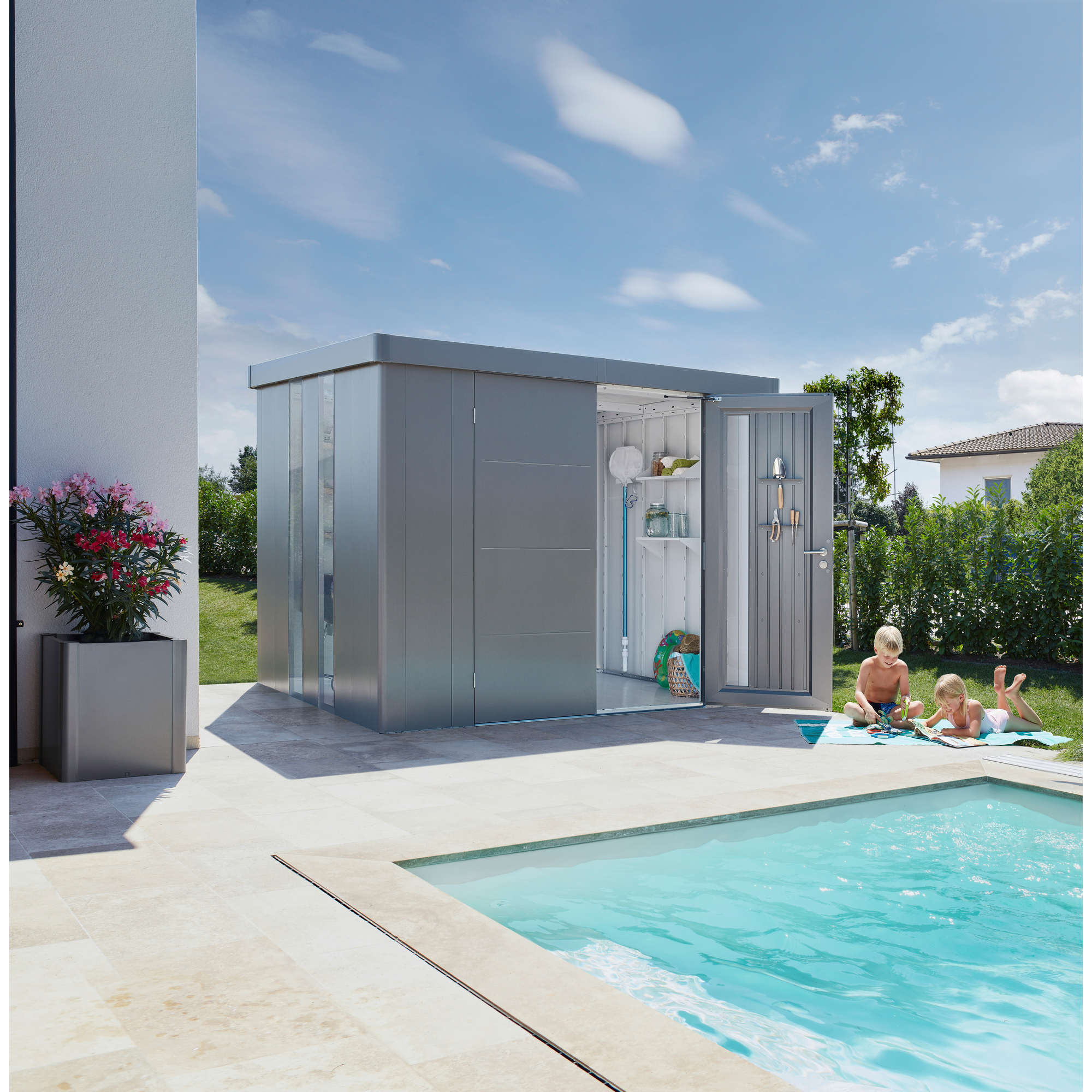 Gerätehaus neben Pool, zwei Kinder lesen am Beckenrand.