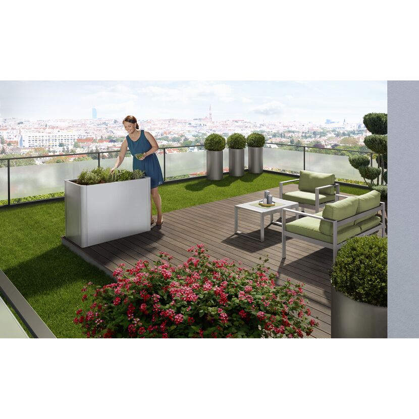 Person pflegt Kräuter in einem Hochbeet auf dem Balkon