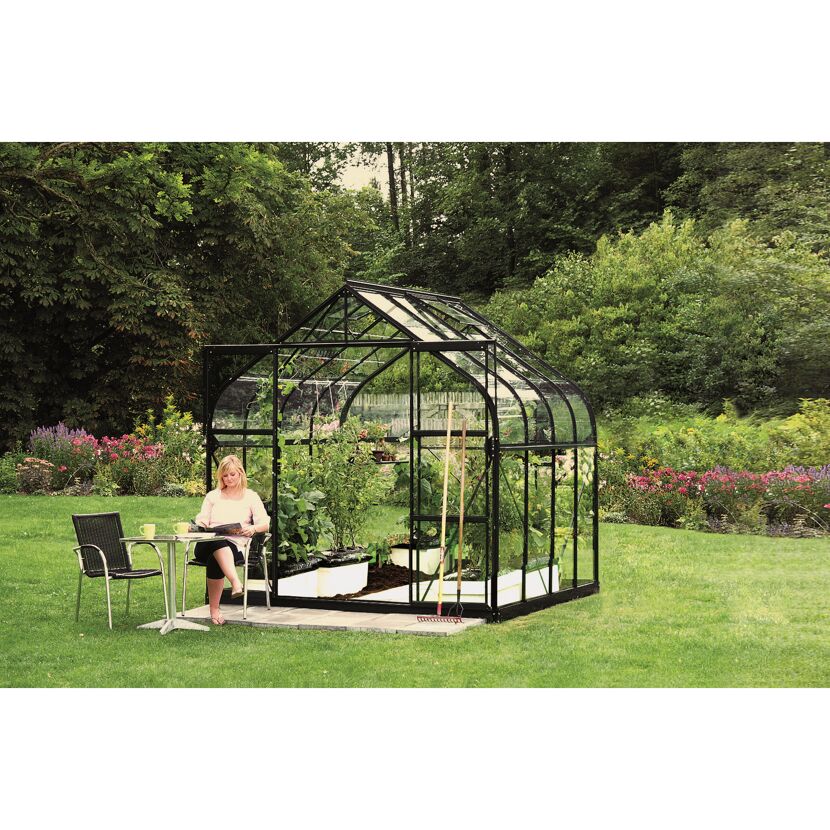 Person sitzt an einem Tisch neben einem Gewächshaus im Garten.