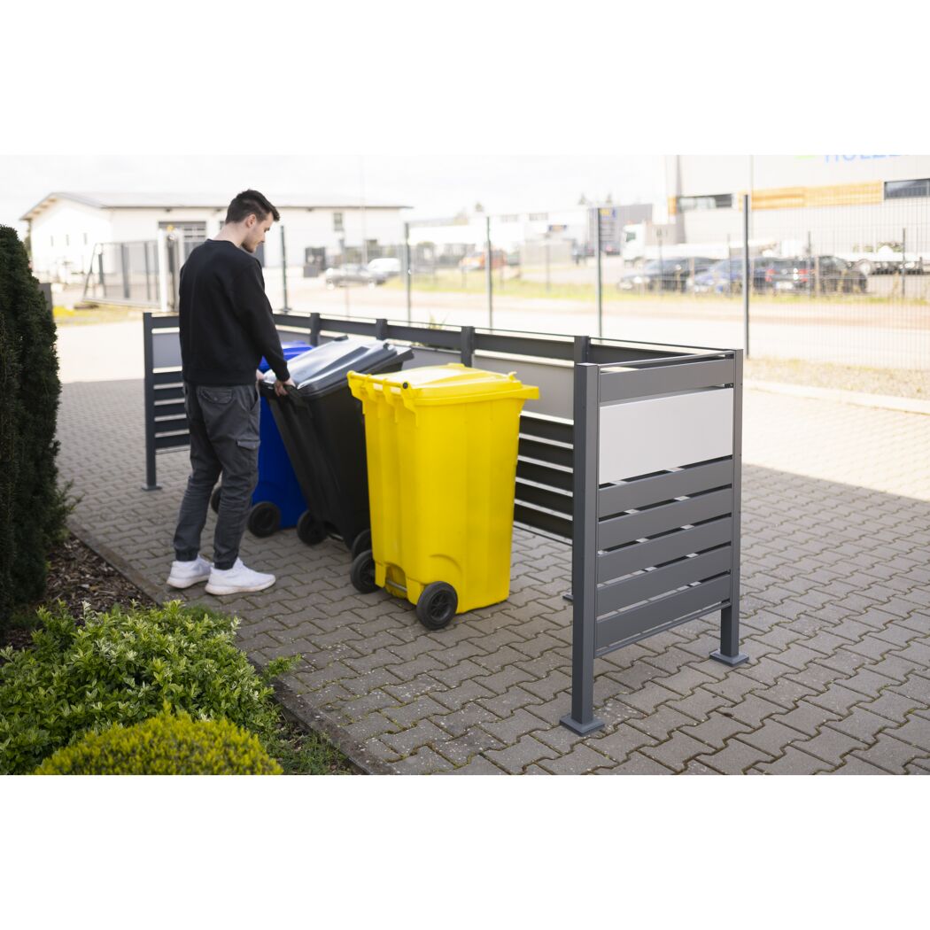 Person schiebt Mülltonne in eine Mülltonnenverkleidung.