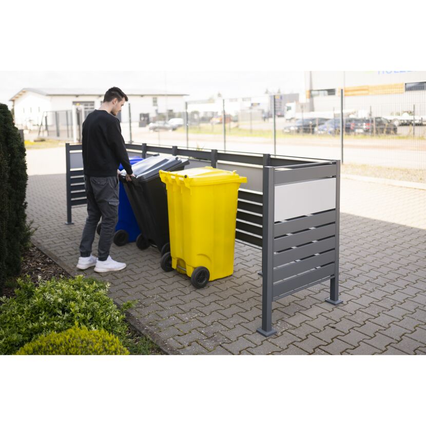 Person schiebt Mülltonne in eine Mülltonnenverkleidung.