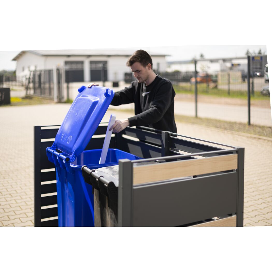 Person wirft Papier in einen blauen Mülleimer