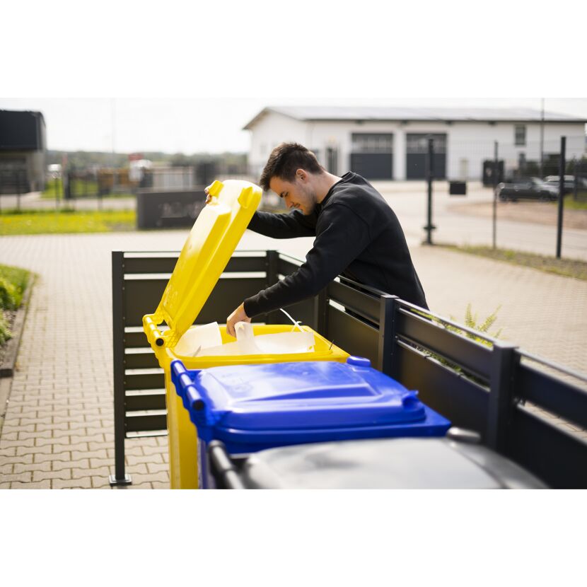 Person wirft Papier in gelbe Mülltonne